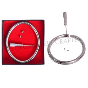 Könnte beinhalten: Ein silberfarbener Metallkragen mit Schraubverschluss, präsentiert in einer schwarzen Box mit rotem Innenraum. Ein Schraubendreher und kleine Schrauben sind enthalten. Der Text "LUXURY STEEL CRAFTS" ist sichtbar.