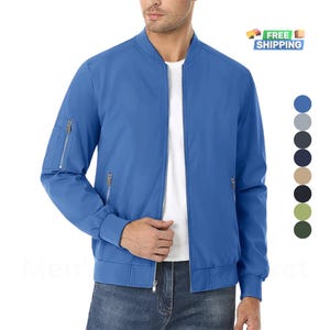 Può includere: Una giacca bomber blu chiaro con chiusura a zip e due tasche con zip sui lati. La giacca ha un colletto e polsini a costine.
