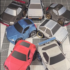 May include: A collection of toy cars in various colors, including black, red, blue, and silver. The cars have detailed features like spoilers and custom wheels. The arrangement showcases a variety of miniature vehicle designs.