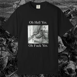 May include: Black t-shirt featuring a grayscale illustration of a large insect on a bed, with the text "Oh Hell Yes." above and "Oh Fuck Yes." below the image. The shirt has a crew neck and short sleeves.