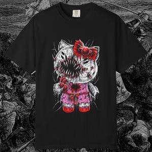 May include: Black t-shirt featuring a graphic of a zombie-like character with a red bow, a gaping mouth, and pink clothing. The design is a mix of cute and horror elements. The shirt has a crew neck and short sleeves.