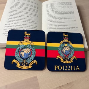 May include: Two navy blue square coasters, each displaying the Gibraltar coat of arms with a globe, crown, and the text "GIBRALTAR" and "PER MARE PER TERRAM". One coaster has the text "PO12211A".