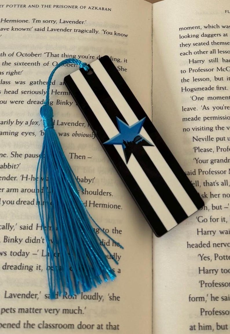 K&ouml;nnte beinhalten: Schwarz-wei&szlig; gestreifter Lesezeichen mit blauem Sterndesign und blauer Quaste. Das Lesezeichen ist rechteckig und zeigt einen Stern mit einer Silhouette im Inneren. Ein dekoratives Accessoire f&uuml;r B&uuml;cherliebhaber.