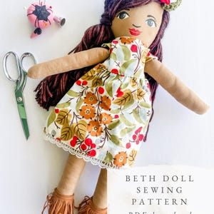 May include: A handmade doll with brown yarn hair, wearing a floral dress with a white lace hem and fringed boots. A floral crown adorns the doll's head. The image also includes a pink pincushion, scissors, and the text "BETH DOLL SEWING PATTERN PDF download."