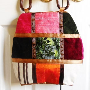 May include: A patchwork tote bag with a variety of colors and textures, including pink, red, green, brown, and white. The bag has a unique design with different fabrics sewn together in a square pattern. The bag has wooden handles.