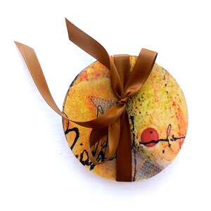 Puede incluir: Conjunto de cuatro posavasos redondos con un diseño abstracto en amarillo, naranja, rojo y negro. Los posavasos están atados con una cinta marrón.