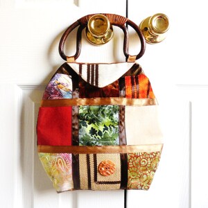 May include: A patchwork tote bag with a brown wooden handle. The bag is made of different fabrics in shades of brown, orange, green, and white. The bag has a large button on the front.