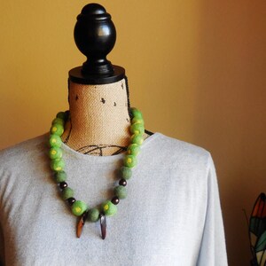 Puede incluir: Un collar de cuentas verdes y amarillas con detalles marrones sobre un maniquí con una camisa gris.