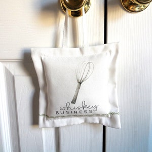 May include: White doorstop with a green whisk and the text "whiskey business" in black.