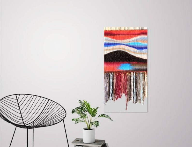 May include: A colourful woven wall hanging with a red, blue and brown colour scheme. The hanging has a fringe border and a textured surface.