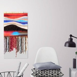 May include: A colourful woven wall hanging with a red, blue and white abstract design. The hanging has a fringe of yarn at the bottom.