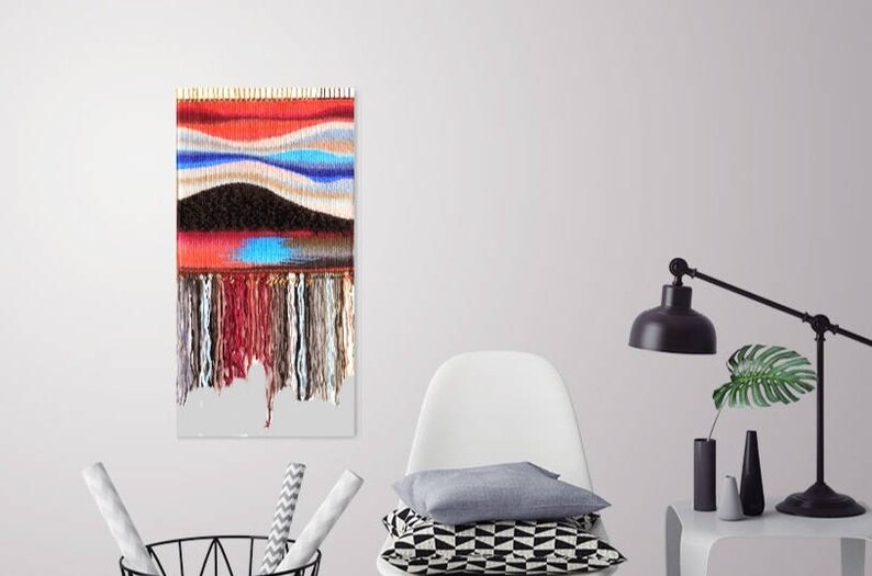 May include: A colourful woven wall hanging with a red, blue and white abstract design. The hanging has a fringe of yarn at the bottom.