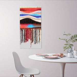 May include: A colourful woven wall hanging with a geometric pattern and fringe. The hanging is made of various colours of yarn, including red, blue, white, and black.