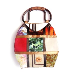 May include: A patchwork tote bag with a brown wooden handle. The bag is made of different fabrics in shades of red, orange, green, brown, and beige. The bag has a button closure.