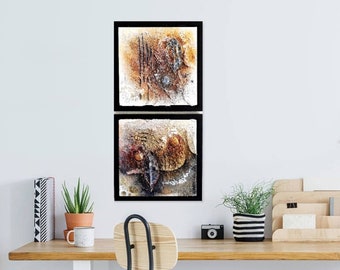 May include: Two framed abstract paintings with a brown, white, and black color scheme. The paintings are in black frames and are hung on a white wall.