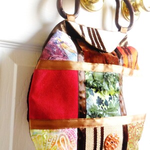 May include: A patchwork handbag with a brown leather handle. The bag is made of different fabrics, including red, green, brown, and white. The bag has a large, round, brown button on the front.