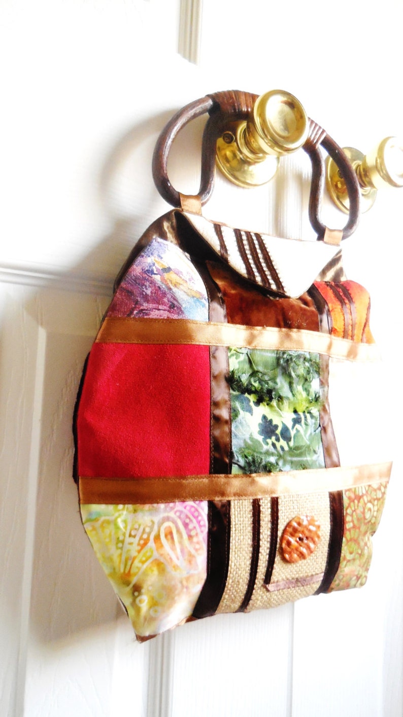 May include: A patchwork handbag with a brown leather handle. The bag is made of different fabrics, including red, green, brown, and white. The bag has a large, round, brown button on the front.