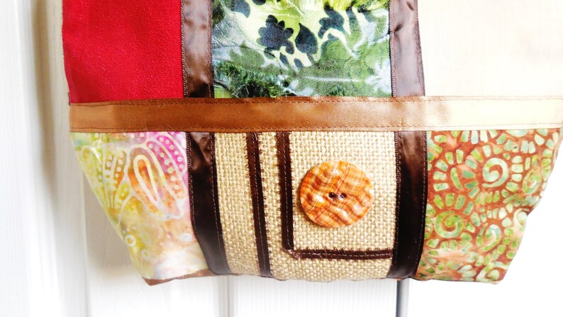 May include: A patchwork tote bag with a brown, beige, and green fabric design. The bag has a brown button and a brown ribbon.