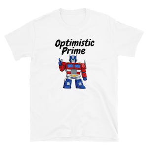 May include: White t-shirt featuring a cartoon illustration of Optimus Prime in red, blue, and silver. The text "Optimistic Prime" is above the character in a black, cursive font.