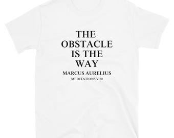 以下が含まれることがあります： 「THE OBSTACLE IS THE WAY」という黒い文字がプリントされた白いTシャツ。作者名、マルクス・アウレリウス、出典、瞑想録V.20も記載。半袖でクルーネックのデザインです。