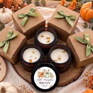 May include: Four brown cardboard gift boxes with green ribbon bows, three amber glass jars containing white candles with wax embeds, and one black candle lid featuring a floral pumpkin graphic and the text Little Pumpkin Baby Levi.
