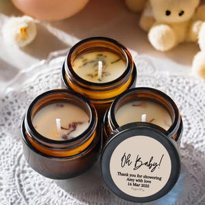 May include: Three small amber glass jars with lids, filled with soy wax candles. The jars have white labels with black text that reads "Oh Baby! Thank you for showering Amy with love 16 Mar 2023".