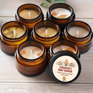 Peut inclure: Un ensemble de sept petits pots en verre ambré contenant des bougies en cire blanche avec des mèches visibles. Le couvercle d'un pot porte une étiquette circulaire avec une illustration de maison en pain d'épices et le texte : CHRISTMAS'S BABY SHOWER, Thank you for coming! 12.03.20xx.