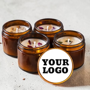 May include: Four amber glass jars containing white wax candles with visible wicks and scattered dried flower petals. A circular white label with a gold border is positioned in the foreground, featuring the black text YOUR LOGO centered.