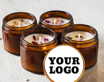 Könnte beinhalten: Vier bernsteinfarbene Gläser mit weißen Wachskerzen, sichtbaren Dochten und getrockneten Blütenblättern. Ein rundes weißes Etikett mit dem schwarzen Text YOUR LOGO befindet sich im Vordergrund und verdeckt teilweise das vordere Kerzenglas.