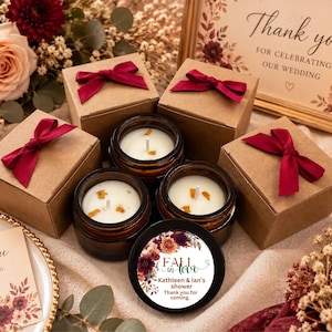 May include: Three amber glass candle jars with white wax and one black lid featuring a floral label that reads Fall in love, Kathleen & Ian's shower, Thank you for coming. Three brown cardboard gift boxes with dark red ribbon bows are included.