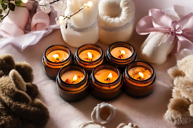 May include: A collection of lit candles in small, brown glass jars. The candles are arranged on a light pink surface, surrounded by decorative items like a plush bear, a wrapped gift, and other candles.