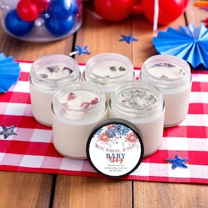 May include: Five small glass jars filled with white wax and topped with dried flower petals. A circular black lid rests in front, featuring a firework graphic and the text: RED, WHITE, & DUE, BABY ABBY, Thank you for celebrating with us, 07.04.20xx.