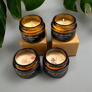 Pu&ograve; includere: Quattro barattoli di vetro ambrato con coperchi contenenti candele profumate. Ogni barattolo ha un'etichetta nera con il testo "Lure Incense Scented Candle".