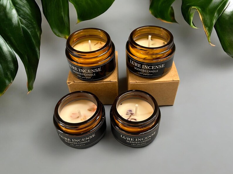 Pu&ograve; includere: Quattro barattoli di vetro ambrato con coperchi contenenti candele profumate. Ogni barattolo ha un'etichetta nera con il testo "Lure Incense Scented Candle".