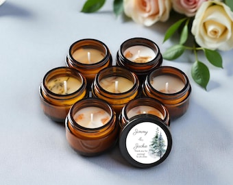 May include: Seven small, round, amber-colored glass jars filled with wax candles. The candles have white wicks and are surrounded by decorative elements. One jar has a black lid with the text "Jimmy & Jackie" and a winter tree design.