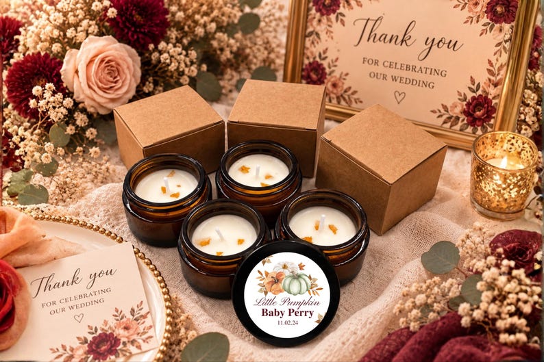 May include: Four amber glass jars filled with white wax candles, each featuring a single wick and small orange accents. One black lid displays a circular label with watercolor pumpkins and the text Little Pumpkin Baby Perry 11.02.24. Three brown cardboard boxes accompany the candles.