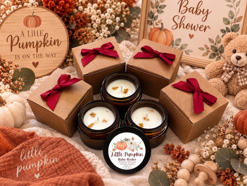 May include: Three amber glass candle jars with white wax and wicks, accompanied by three matching brown cardboard gift boxes tied with deep red satin ribbons. One black candle lid features a pumpkin graphic and the text Little Pumpkin Baby Ryder.