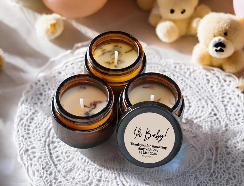 May include: Three small amber glass jars with lids, filled with soy wax candles. The jars have white labels with black text that reads "Oh Baby! Thank you for showering Amy with love 16 Mar 2023".