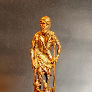 Könnte beinhalten: Eine goldfarbene Metallglocke mit einer detaillierten Skulptur eines Hirten mit einem Stab und Schafen. Die Glocke hat einen pyramidenförmigen Sockel.