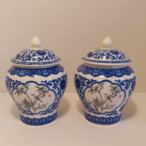 May include: A pair of blue and white porcelain jars with lids. The jars have a floral design and a bird on a branch.