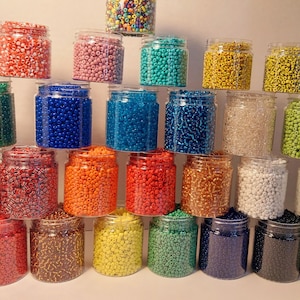 May include: A collection of small, clear jars filled with colorful beads. The beads are in various colors, including red, pink, green, blue, yellow, orange, and white. The jars are arranged in a pyramid shape.
