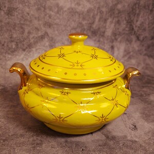 May include: A yellow ceramic soup tureen with gold accents and a lid. The tureen has a floral design and is decorated with gold dots.