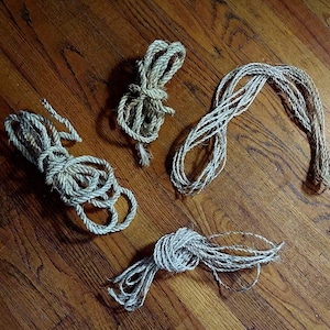 Puede incluir: Cuatro carretes de cuerda de fibra natural, cada uno atado de forma diferente, sobre una superficie de madera.