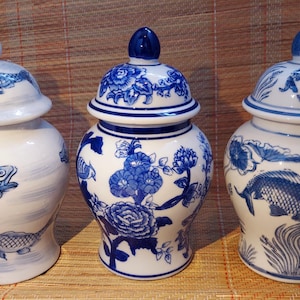 Pode incluir: Três jarros de cerâmica branca com desenhos florais e de peixes azuis e brancos. Os jarros têm tampas e são decorados com desenhos florais e de peixes azuis e brancos.