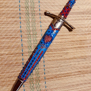 May include: A decorative dagger with a silver blade and guard. The handle and sheath are blue, adorned with red and blue rhinestones. A red heart design is centered on the sheath. The dagger is approximately 14 inches long.