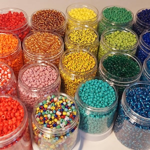 May include: A selection of clear plastic jars filled with small beads in a variety of colours. The beads include shades of red, orange, yellow, green, blue, and white. Some jars contain mixed colours. Suitable for jewellery making and crafts.