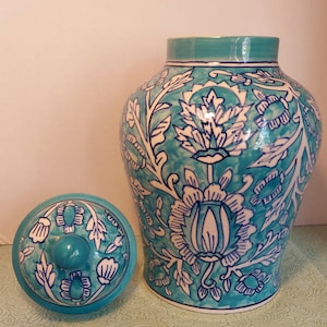 May include: A turquoise ceramic jar with a matching lid. The jar and lid are decorated with white floral patterns. The jar is approximately 10 inches tall and 8 inches wide.
