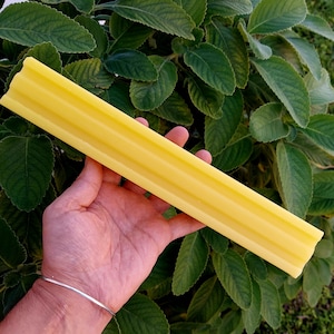 May include: A long, yellow bar of soap with a ridged texture. The soap is being held in a hand.