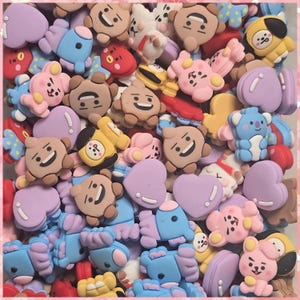 May include: A collection of colorful, cartoon-style charms in various shapes, including hearts, stars, and character figures. The charms are primarily pastel shades of pink, blue, yellow, and brown, with white accents and smiling faces.