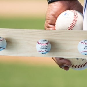 May include: A wooden baseball display board with three baseballs attached. The baseballs are white with red stitching and the words "OFFICIAL LEAGUE" printed on them. The board is held by a person.